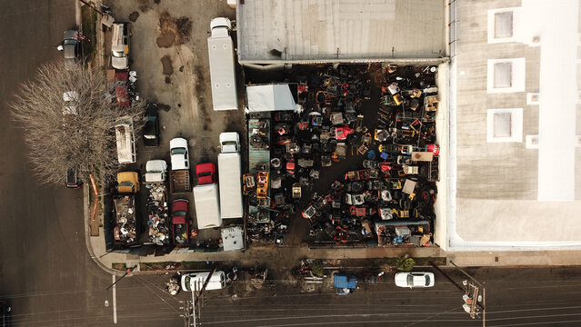 Aerial view of an industrial salvage yard filled with scrap metal, discarded machinery, and various vehicles parked in a lot in Los Angeles, California, United States.