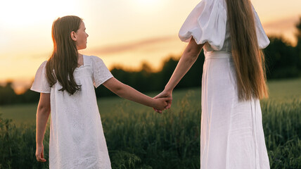 Two girls in white dresses holding hands in a field at sunset © shine.graphics