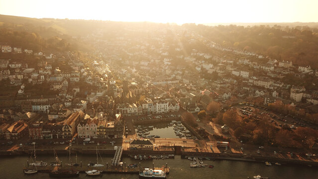 Aerial view of the historic town of Kingswear with boats in the harbor, stone buildings, and warm golden hour sunlight illuminating the hillside in Kingswear, England, United Kingdom.