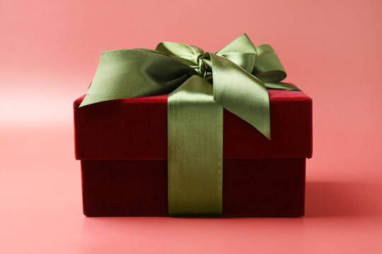 Gift box with green satin bow on red background, closeup