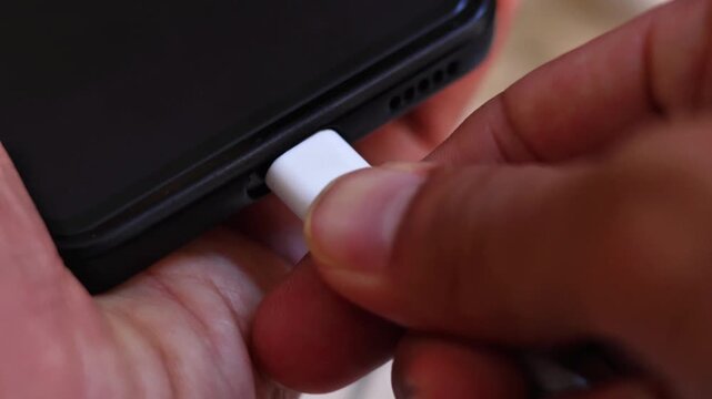close up of hand inserting a white USB Type-C cable into a smartphone charging port, mobile phone battery connection concept.