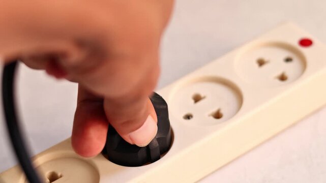 Close up of hand plugging a black power adapter into a white extension cord outlet, electricity and charging laptop concept.