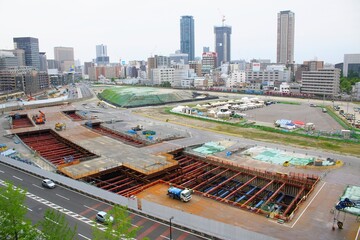 都市再開発の大規模な建築工事現場と高層ビル群の風景 © JtO