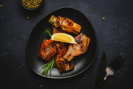 Fried artichoke hearts on black textured dinnerware with dark knife and fork. Gourmet restaurant catering and wholesome plant based dieting concept, horizontal flat lay.