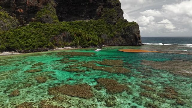 Drone footage of a catamaran anchored in turquoise waters beneath the cliffs of Fronton Beach.