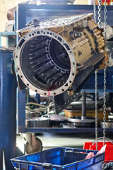 Fototapeta premium A heavy industrial yellow transmission unit with open valve body mounted on a blue fixture stand inside a workshop.