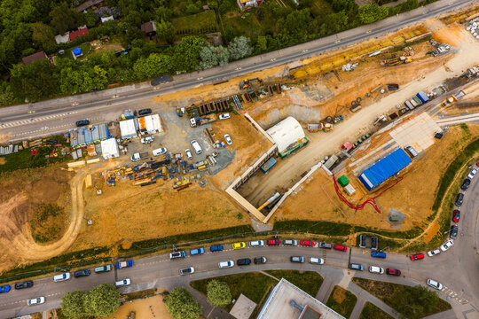 Aerial view of a construction site featuring excavation work, heavy machinery, and temporary site containers adjacent to a busy road with traffic in Brno, South Moravian Region, Czechia.
