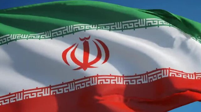 National flag of iran waving in the wind against a clear blue sky