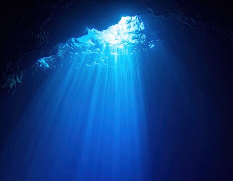 Sunlight beams penetrating surface of underwater cave, dramatic light rays filtering through clear blue water, cavern entrance opening to sky above, deep ocean.