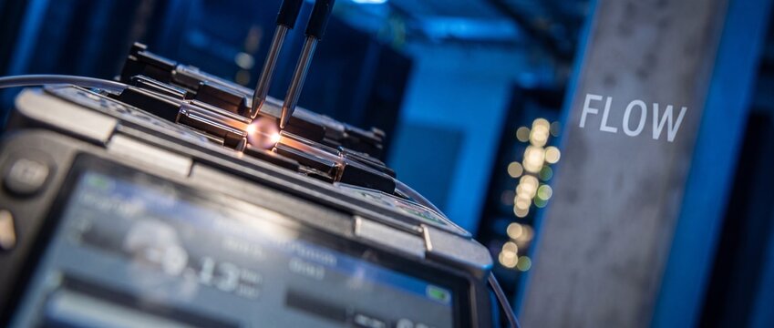 Fiber optic fusion splicer connecting glass cables in server room with bright electric arc, data center infrastructure technology concept representing fast internet network flow and communication.