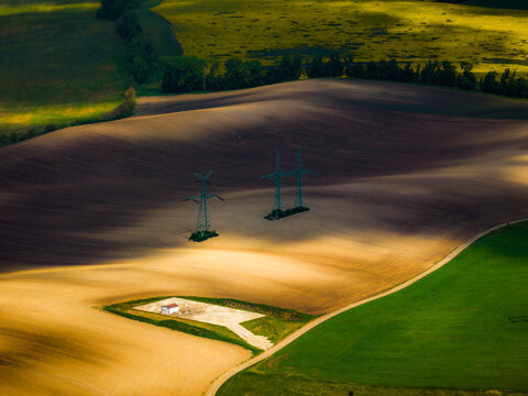 Aerial view of rolling agricultural fields with power pylons and a small utility building in the South Moravian countryside near Brno, South Moravian Region, Czechia.