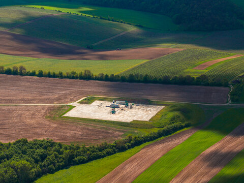 Aerial view of a small industrial facility situated on a concrete pad amidst rolling agricultural fields with patches of green and brown crops in Brno, South Moravian Region, Czechia.