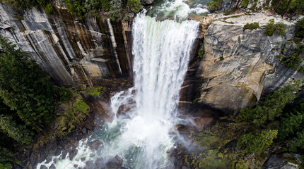 Fototapeta premium Spectacular Cinematic Aerial Shot Of Massive Waterfall Plunging Over High Sheer Cliff Into Mist Pool