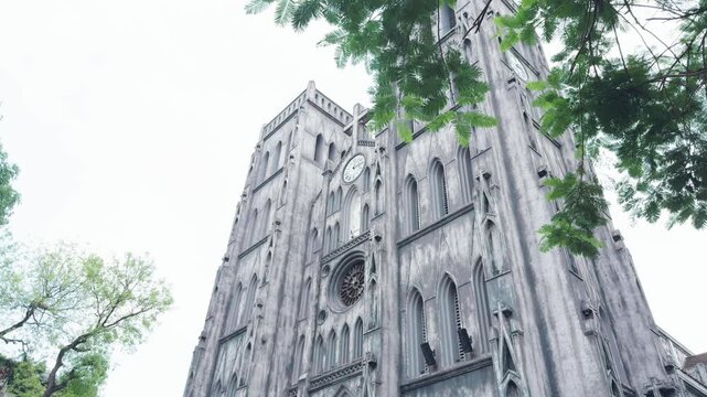 St. Joseph's cathedral, a neo gothic catholic church landmark in hanoi, vietnam, displaying its weathered facade and prominent architectural details with palm trees framed by a metal fence