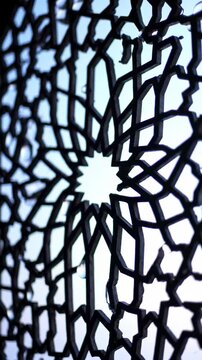 Intricate geometric star pattern in dark metal, backlit by a soft blue sky, creating a traditional Islamic architectural detail, ornamental screen