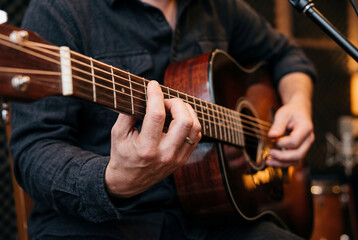 Obraz premium Musician wearing a dark shirt sitting in a recording studio playing a brown acoustic guitar