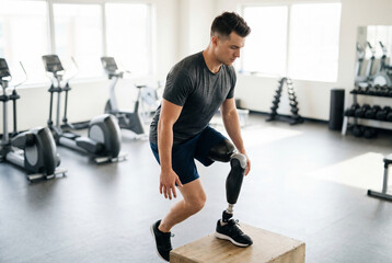 Fototapeta premium Man with prosthetic leg doing box jump exercise in modern gym