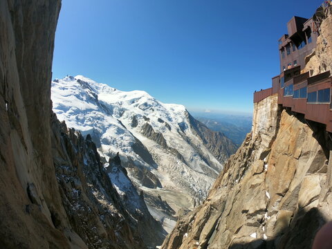 Aerial view of the Aiguille du Midi station perched on rocky cliffs in the French Alps, overlooking the snow-capped Mont Blanc massif in Chamonix, Auvergne-Rhone-Alpes, France.