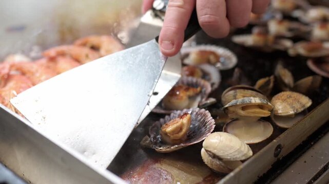 Close up of a professional cook grilling mixed seafood. Fresh prawns, clams, and scallops sizzling on a hot commercial kitchen griddle