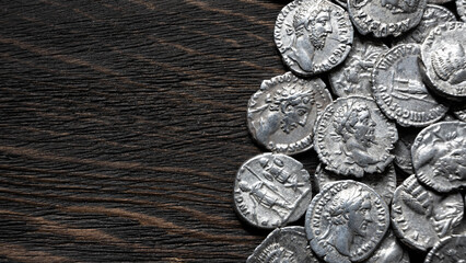 Collection of ancient Roman silver coins on a dark wood background, top view. Antique denarii with emperor portraits. Archaeology and numismatics concept. Copy space for text © scaliger