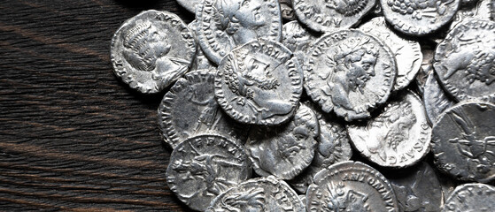 Top view of ancient silver coins on a dark wooden board. Old Roman currency hoard flat lay. Panoramic banner for money and antique concept © scaliger