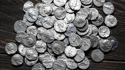Collection of ancient Roman silver coins on a dark wooden table. Pile of authentic denarii with portraits of emperors, top view, for antique vintage background © scaliger