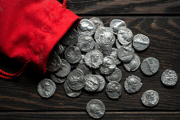 Red cloth bag spilling ancient Roman silver coins on a dark rustic wooden table. Top view of historical currency and treasure concept. Flat lay of numismatic money © scaliger