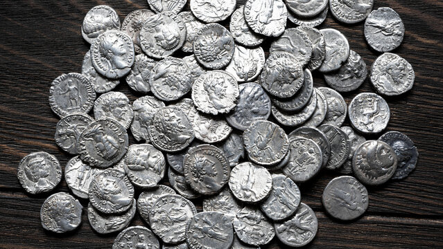 Collection of ancient Roman silver coins on a dark wooden table. Pile of authentic denarii with portraits of emperors, top view, for antique vintage background
