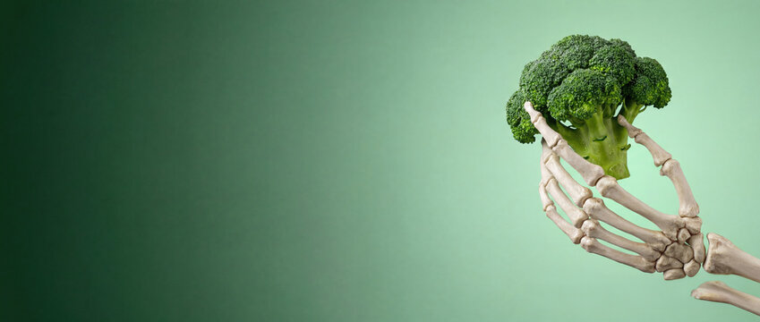 Human skeleton hands holding fresh green broccoli cabbage head on green background with copy space
