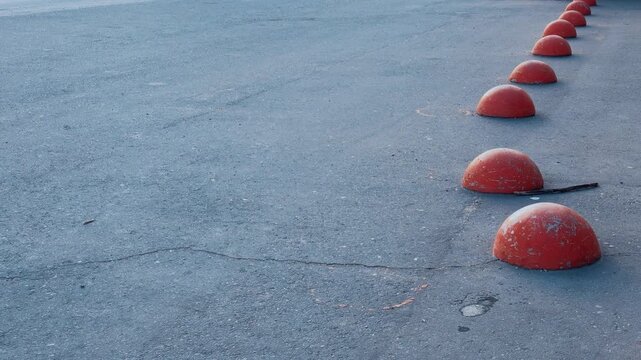 Red hemispheres on asphalt pedestrian path, row of weathered orange bollards creating rhythmic barrier in empty urban pedestrian