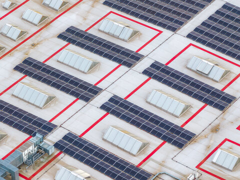 Aerial view of solar panels installed on a flat industrial roof with multiple skylights and red safety markings in Breclav, South Moravian Region, Czechia.