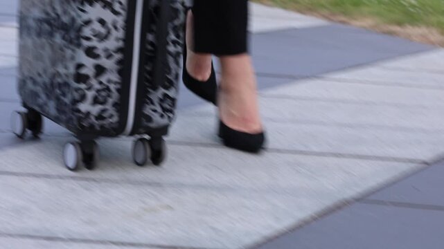 Woman walks with suitcase on city path while wearing high heels in afternoon light