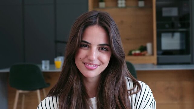 Charming young woman with a radiant smile and long brown hair looking directly at the camera. Her genuine expression conveys happiness and confidence, set against a modern kitchen backdrop at home