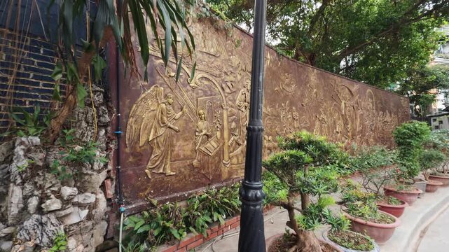 St. Joseph's cathedral courtyard wall featuring intricate bas relief sculpture depicting religious figures and scenes, surrounded by potted plants and natural greenery in hanoi, vietnam