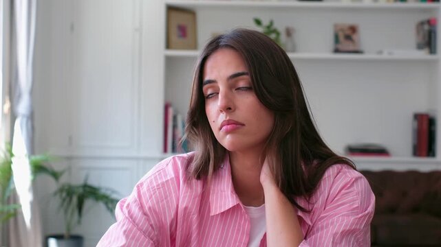 Unhappy and thoughtful young brunette woman looking out a window, feeling lonely and melancholic while sitting in her living room, lost in sad thoughts about her personal problems