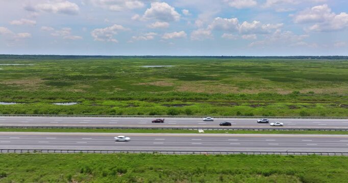 Florida I-75 corridor passing through Everglades-like wetlands under direct sun with cars and semi-trucks in transit.