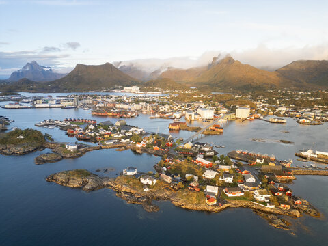 Aerial view of Lofoten islands featuring colorful houses on rocky islets connected by bridges with mountains in the background in Sund, Nordland, Norway.