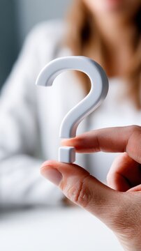 Person holding a white question mark symbol between fingers representing inquiry curiosity and seeking answers concept with blurred background