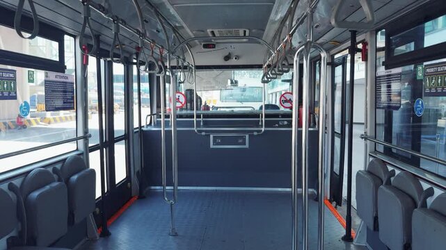 Modern airport shuttle bus interior featuring empty rows of gray seats, polished chrome handrails, and wide windows revealing the sunny terminal, depicting public transportation and travel readiness