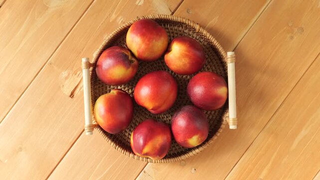 Rotating wicker basket of fresh nectarines on a wooden table