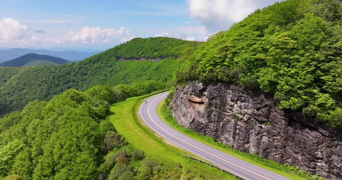 Athletic bicyclist climbs steep Blue Ridge Parkway road, surrounded by forested hills, summer sunlight and breathtaking Appalachian scenery.