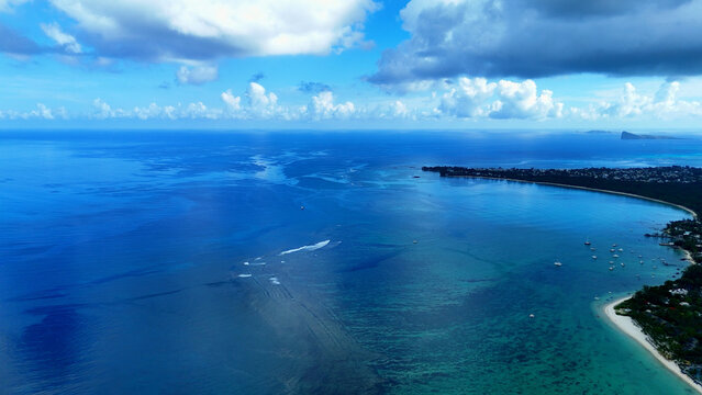 Aerial view of turquoise waters, coral reefs, and sandy coastline with small boats anchored near the shore under a blue sky in Trou-aux-Biches, Pamplemousses District, Mauritius.