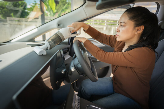 woman using portable handheld vacuum cleaner to clean dust on an electric car dashboard