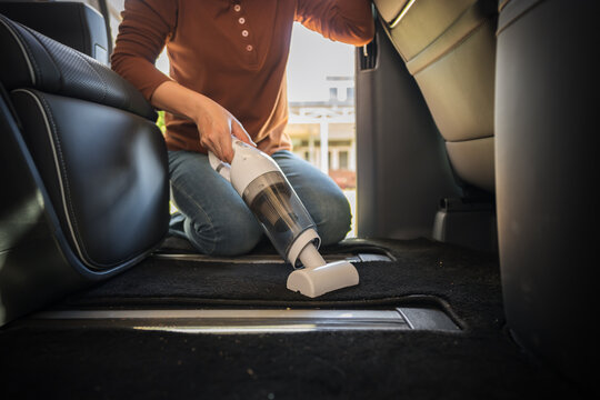 close up hand of woman using portable handheld vacuum cleaner to cleaning the floor mat of her luxury car