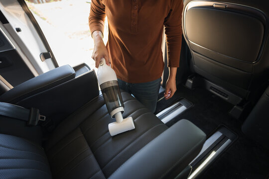 close up hand of woman using portable handheld vacuum cleaner to clean dust on leather car seat of electric car