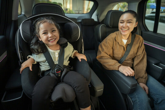happy mother take care her preschool girl in car seat. play and talking with child