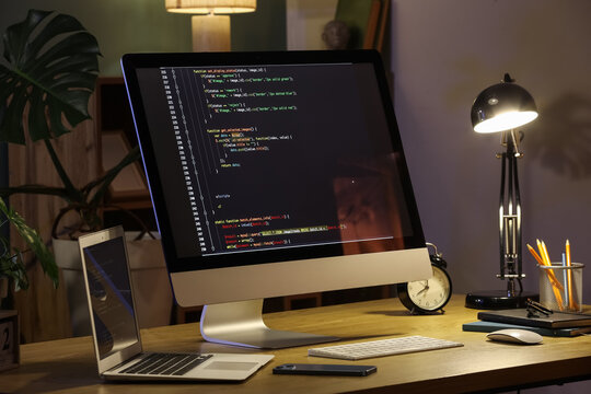 Programmers workplace with computer, laptop and glowing lamp in dark office
