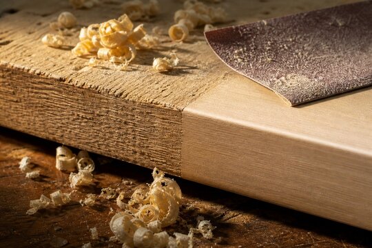 Sandpaper on a wooden board edge with wood shavings, contrasting raw and finished surfaces.