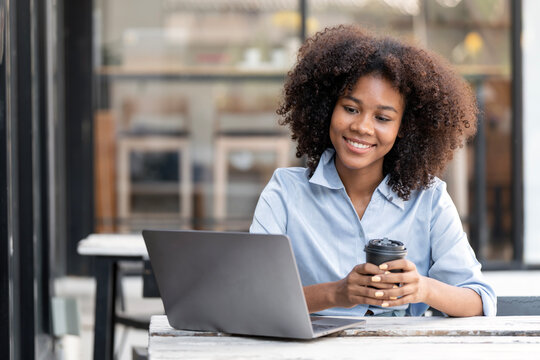 Smiling young African American woman holding coffee cup and looking at laptop