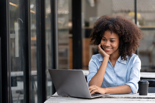 Smiling young African American woman working on laptop at outdoor cafe